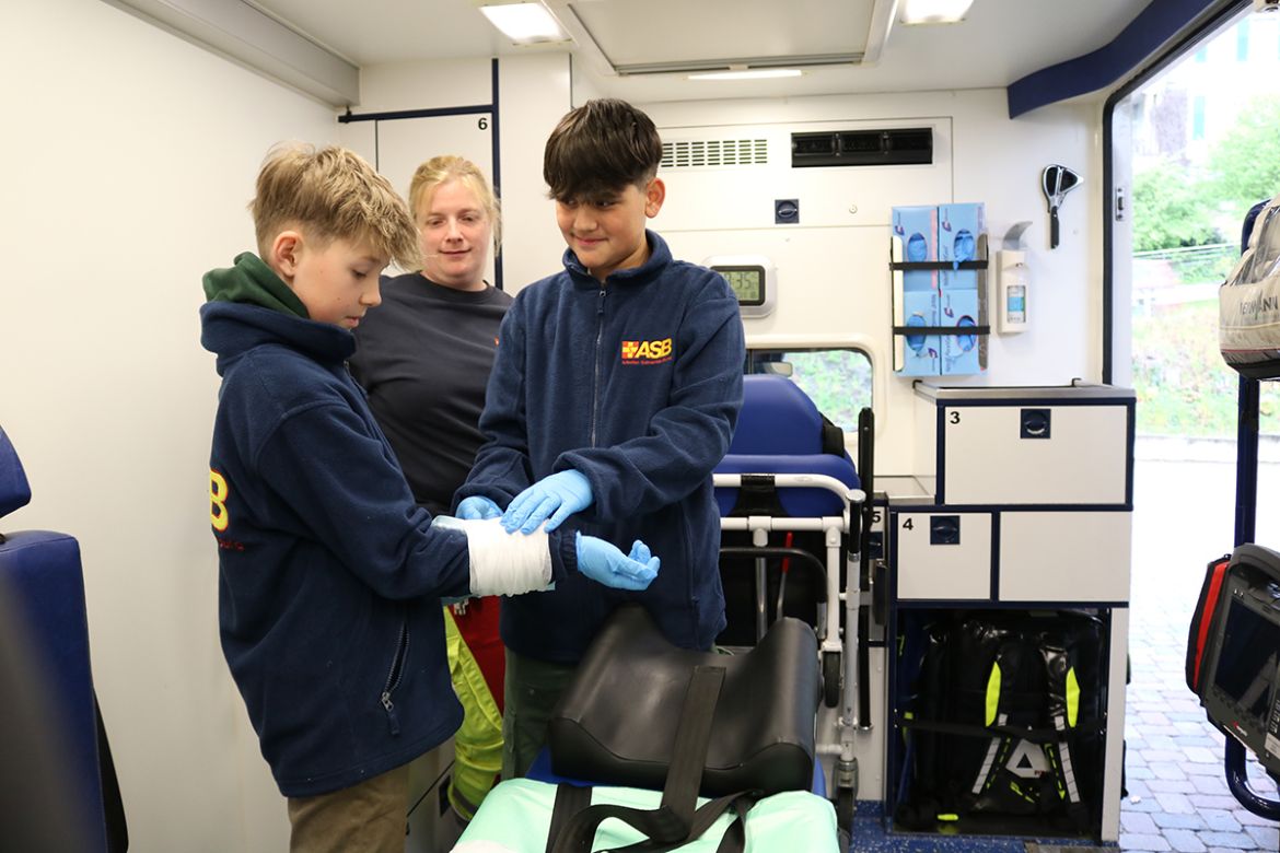 Im ASB-Rettungswagen: Die Schüler Nick (li.) und Minel übten beim Zukunftstag zusammen mit Rettungssanitäterin Katrin Decker, wie man eine Kältekompresse mit einer Mullbinde anlegt.